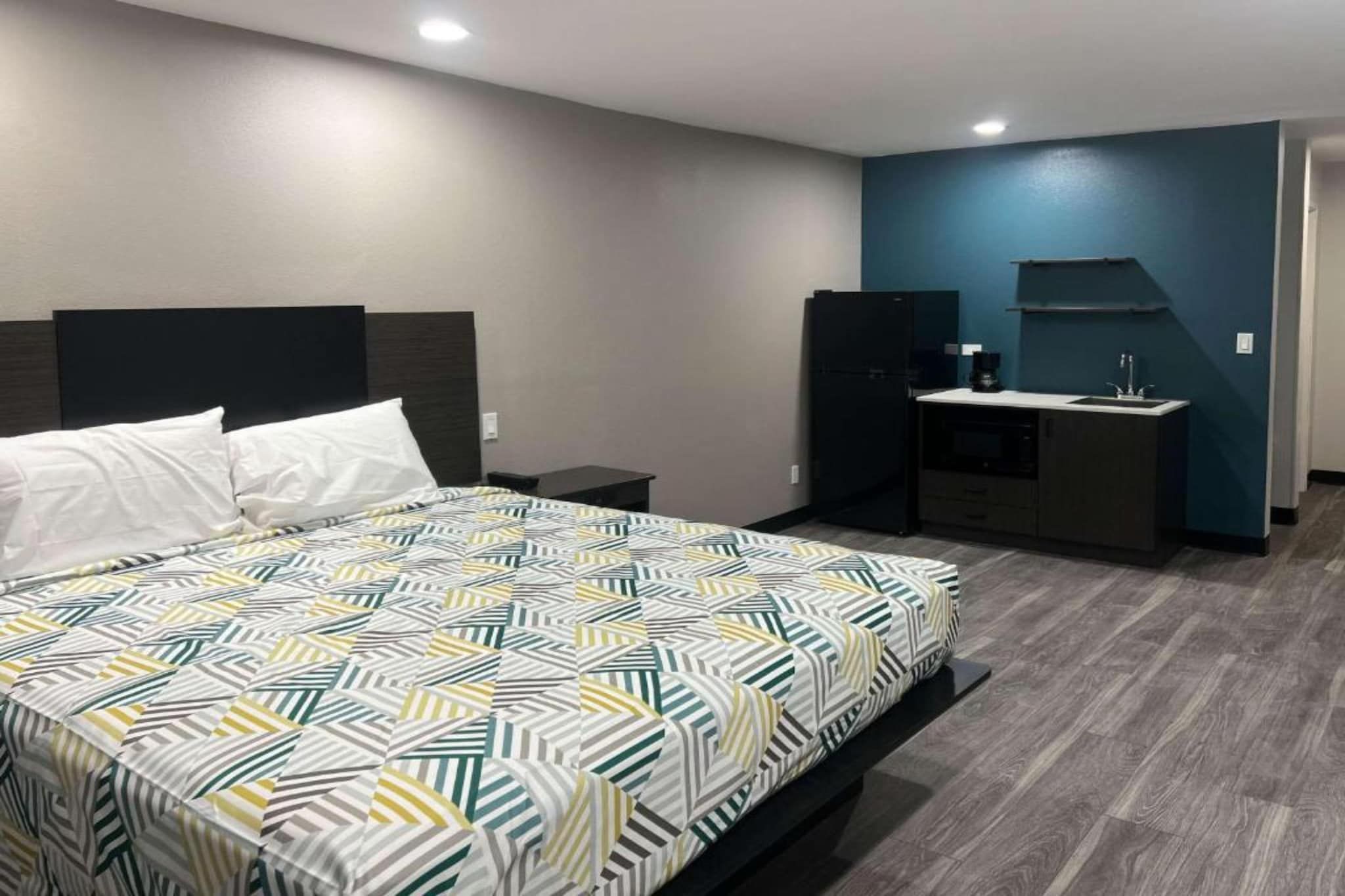 Ein Hotelzimmer mit einem Bett, einem kleinen Schreibtisch, einem Kühlschrank und einer Küchenzeile.