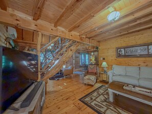 A wooden interior with a staircase, a television, a sofa, and a lamp.