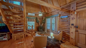 L’intérieur d’une cabane en rondins, avec un escalier en bois, une cheminée, un canapé et une porte.