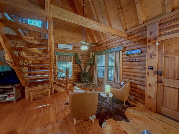 A log cabin interior with a wooden staircase, a fireplace, a sofa, and a door.