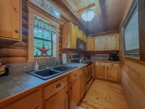 A wooden cabin interior with a kitchen area, including a sink, stove, and cabinets.