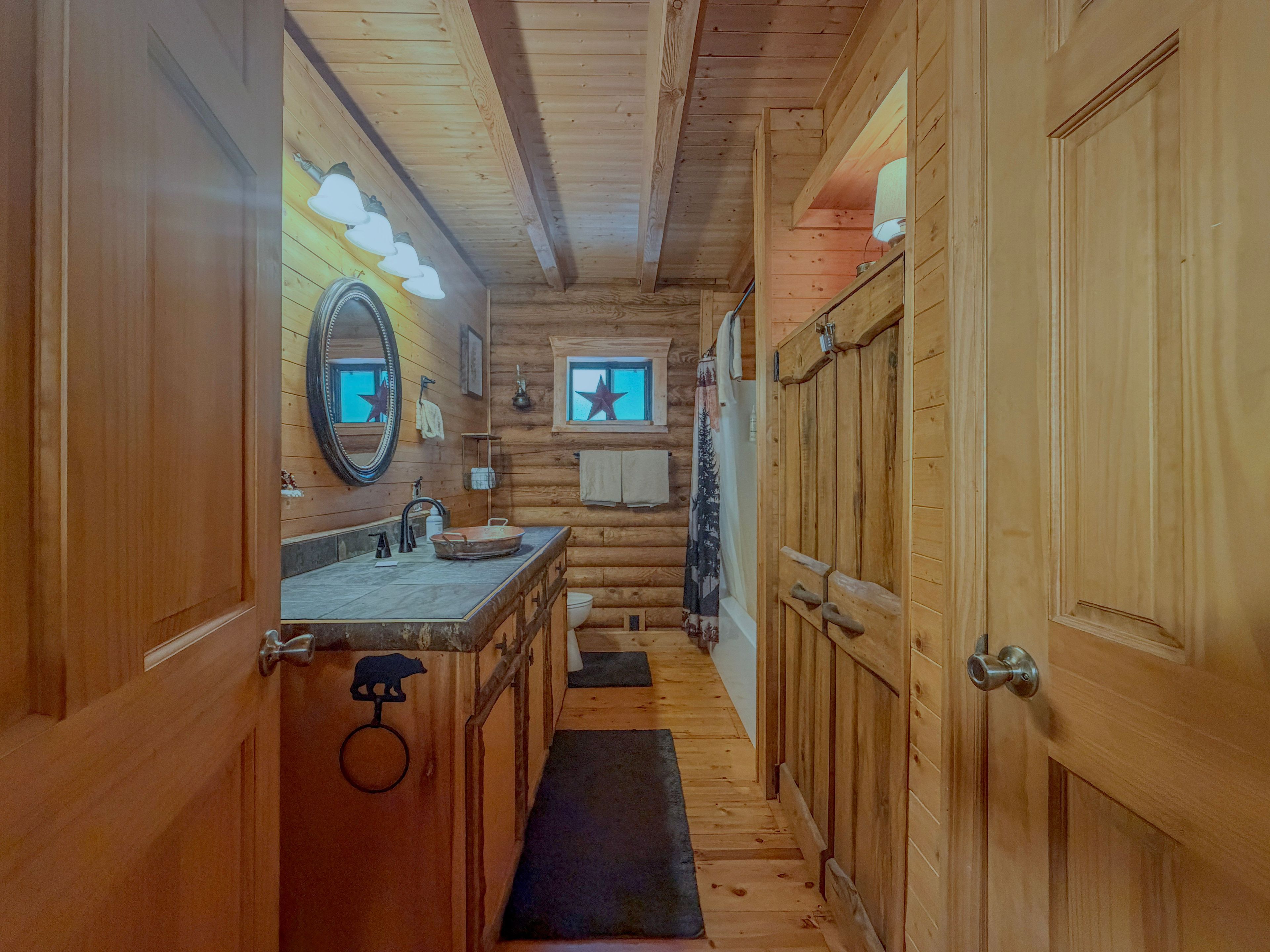 Interieur van een houten blokhut met een badkamer, voorzien van een wastafel, spiegel en raam met stersieraden.
