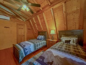 A cabin bedroom with two beds, wooden walls, a ceiling fan, and a nightstand with a lamp. - Mountain Cabin | Hot Tub & Deck | Mountain Views (Tiger)