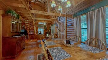 L’intérieur d’une cabane en rondins, avec un coin repas, des meubles en bois et un lustre.