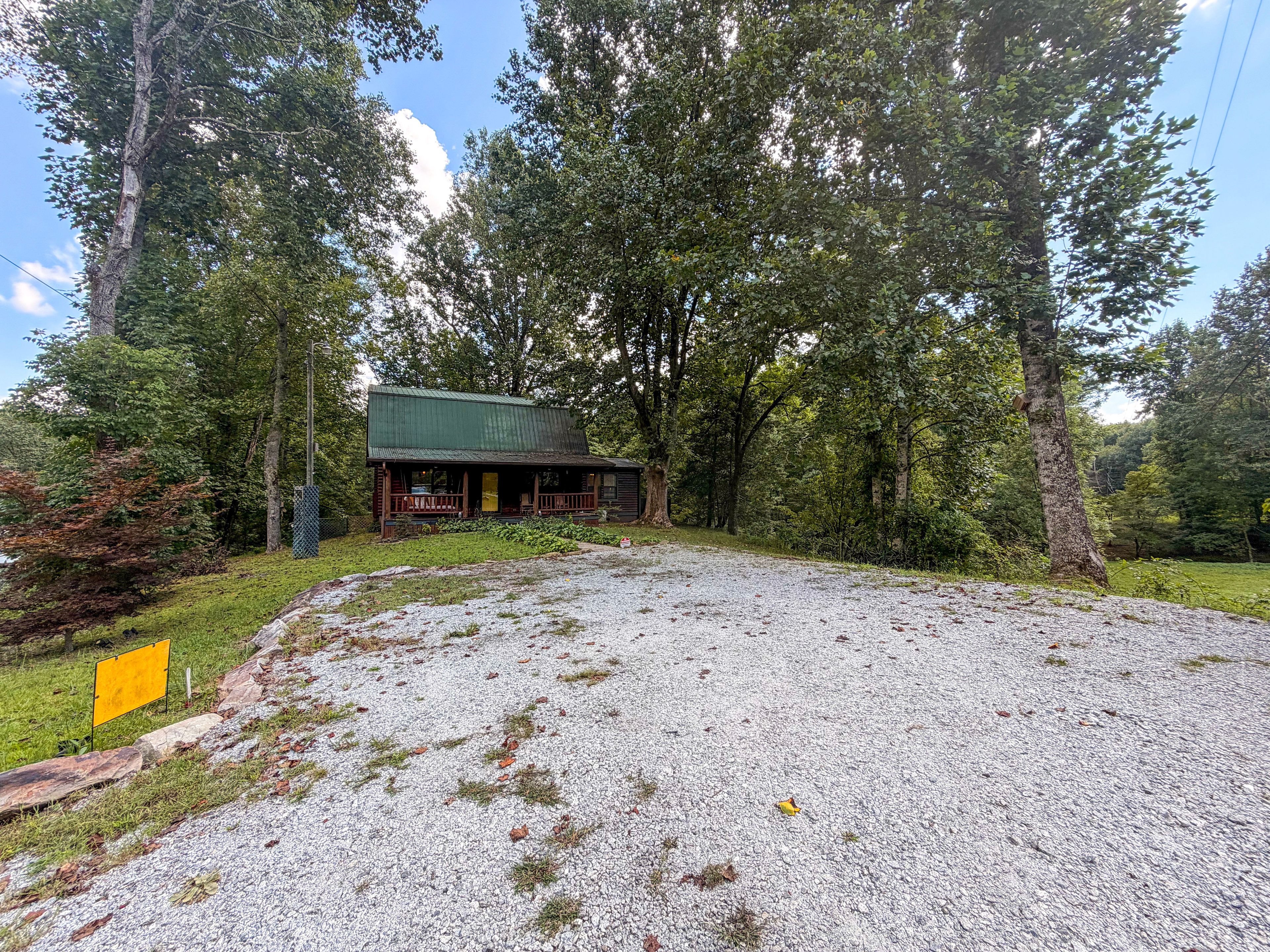 A rustic cabin with a gravel driveway, surrounded by dense trees.