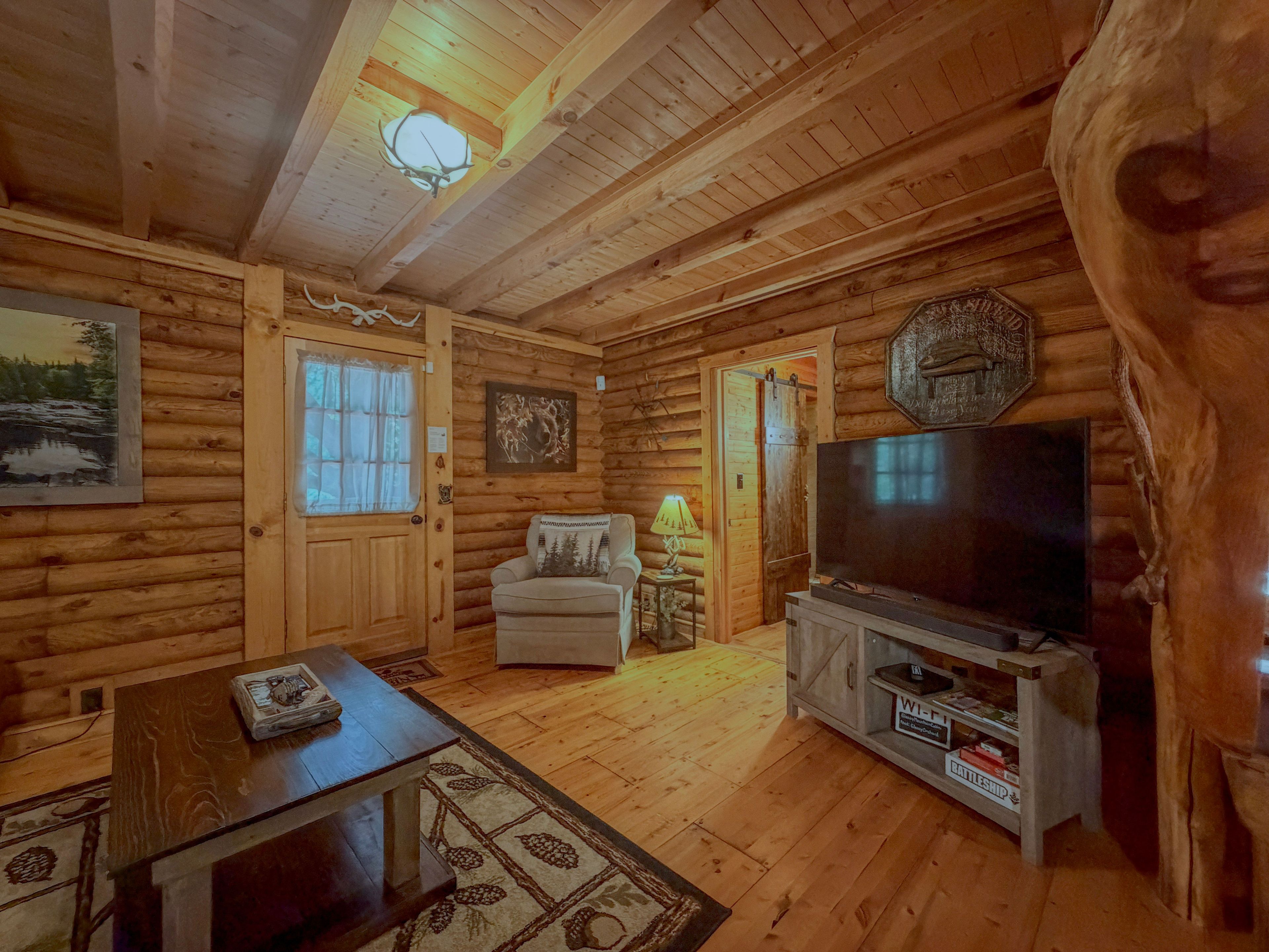 L'intérieur d'une cabane en rondins, avec une télévision, une cheminée, une porte avec une fenêtre et un tableau encadré au mur.