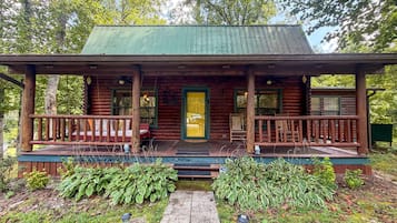 Une cabane en rondins avec un porche, une pancarte de bienvenue et une porte verte.