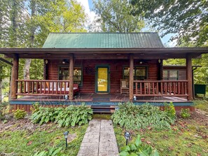 A log cabin with a porch, a welcome sign, and a green door.
