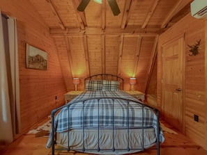 A cozy room with a bed, two bedside lamps, a wooden ceiling, and a door with a deer head decoration.