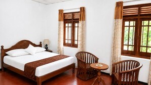 A hotel room with a wooden bed, two wooden chairs, a small round table, and windows with curtains. - PiyaSewana Spice Garden Villa is located close to Colombo Katunayake Airport, (Banduragoda)