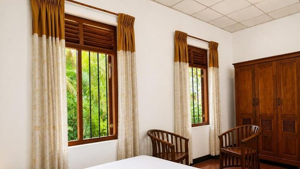 A hotel room with a bed, two chairs, a wardrobe, and windows with curtains. - PiyaSewana Spice Garden Villa is located close to Colombo Katunayake Airport, (Banduragoda)