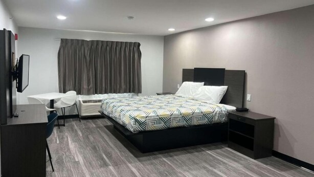 Ein modernes Hotelzimmer mit Bett, Schreibtisch, Sessel und Fernseher.