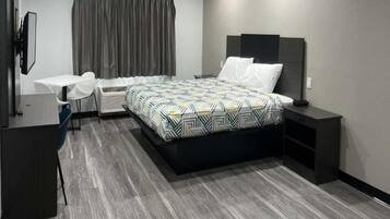 Quarto de hotel moderno com cama, mesas de cabeceira, escrivaninha e uma cadeira.