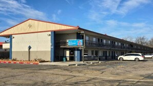 Un motel avec un toit rouge, une enseigne bleue indiquant le numéro de chambre 6 et un parking où sont garées deux voitures.