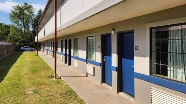 Un bâtiment avec une rangée de portes, chacune surmontée d’une fenêtre. Une voiture est garée dans l’allée.