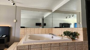 Ein modernes Badezimmer mit einer großen Badewanne, einem Spiegel und einer Topfpflanze.