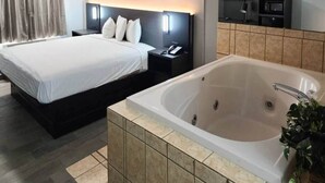 Ein Hotelzimmer mit einem großen Bett, einem Nachttisch mit Telefon, einem kleinen Tischchen und einem separaten Badezimmer mit Badewanne.