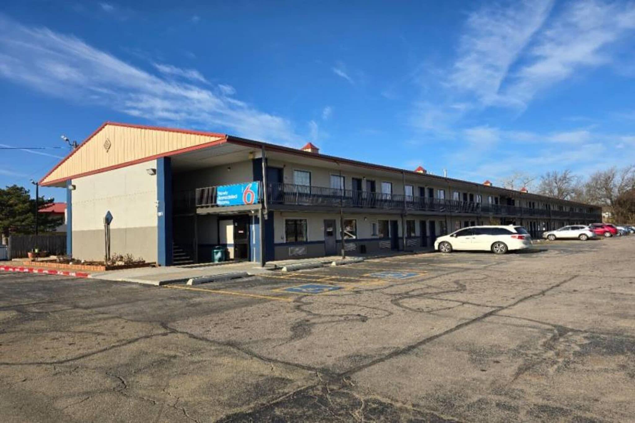 A motel with a single-story structure, a parking lot, and a clear sky.
