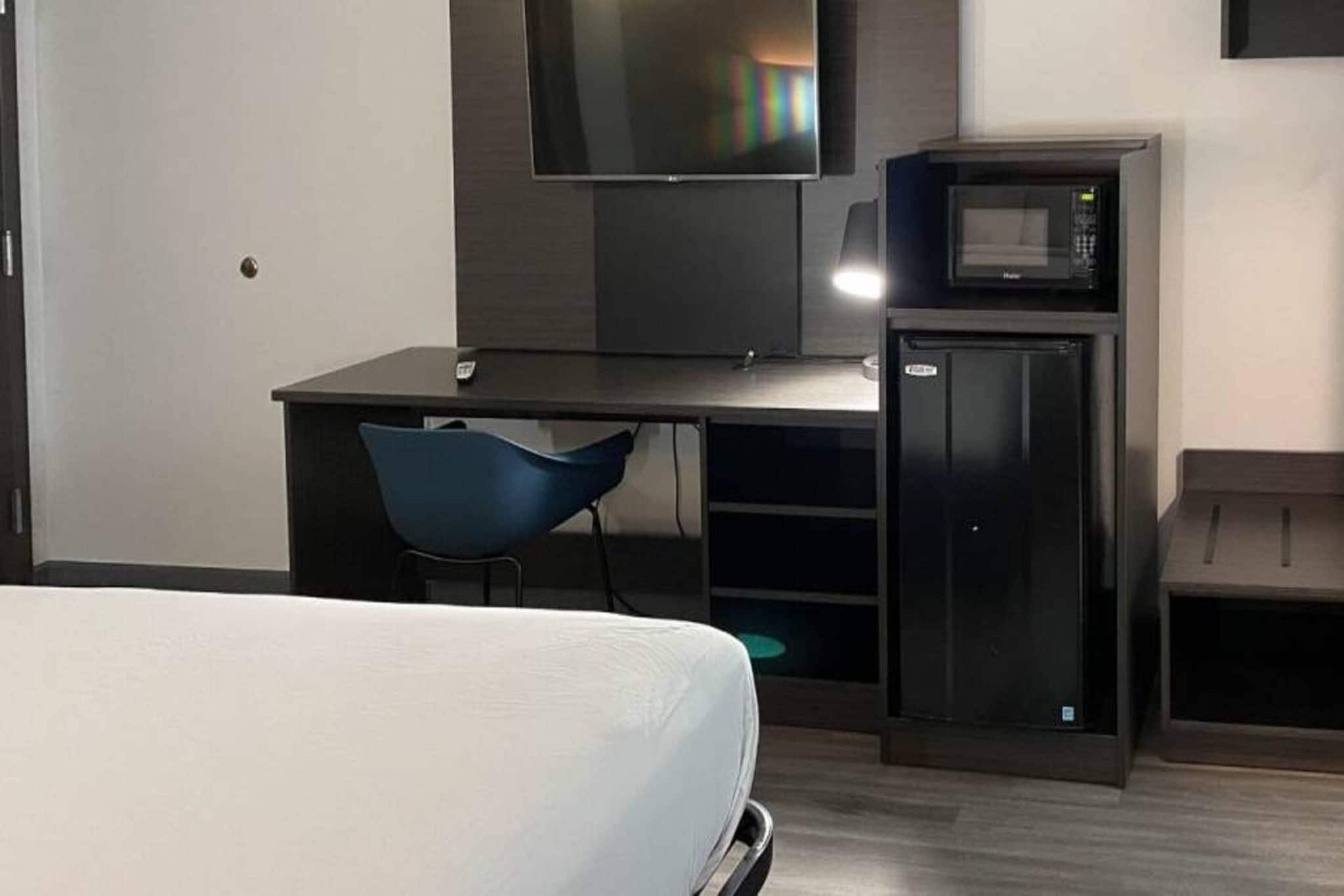 A hotel room with a bed, a desk with a chair, a television, and a minibar.