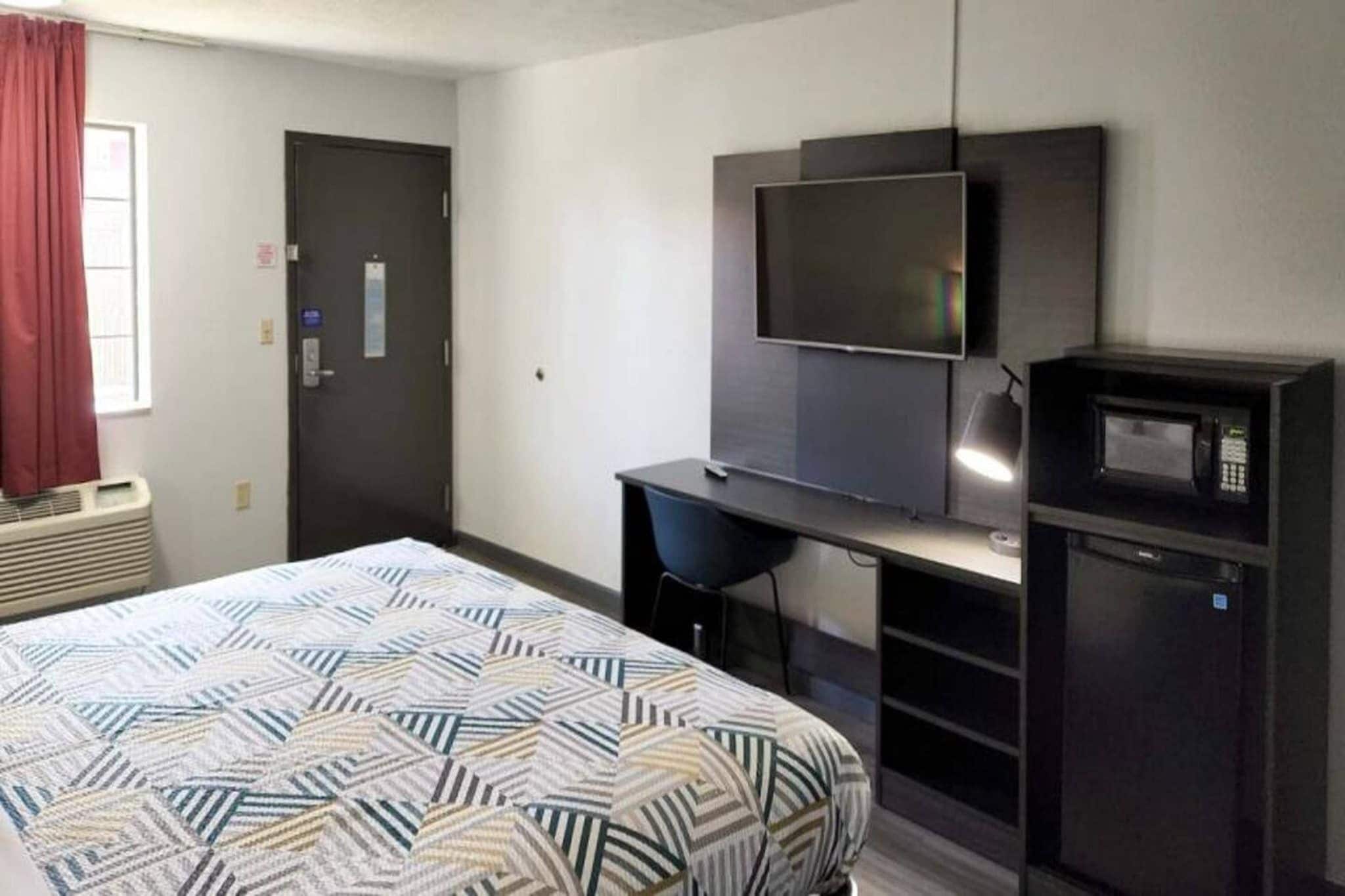A hotel room with a bed, a desk, a television, and a microwave.