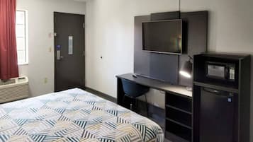 A hotel room with a bed, a desk, a television, and a microwave.