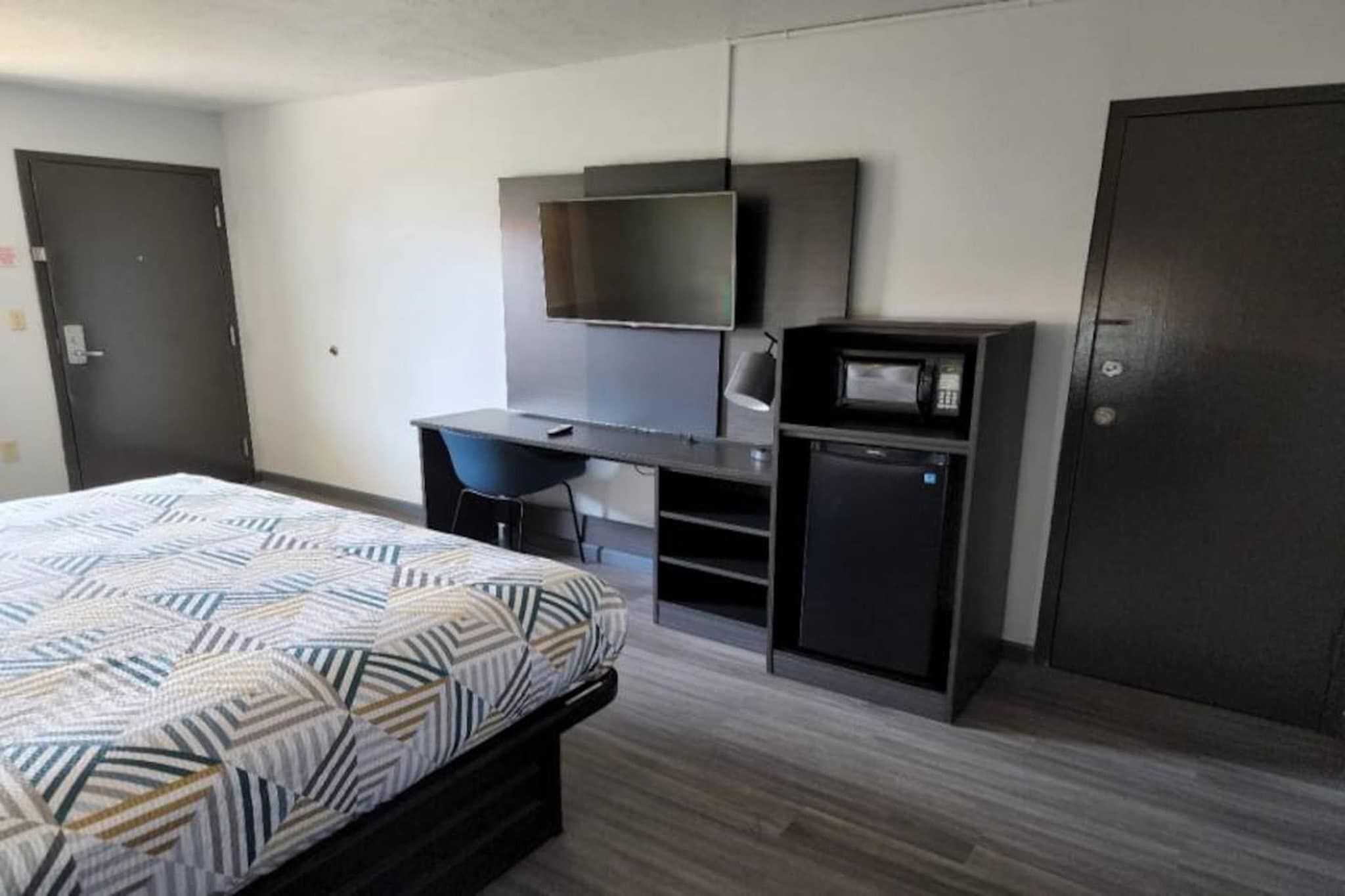 A bedroom with a bed, a desk, a television, a microwave, and a wardrobe.