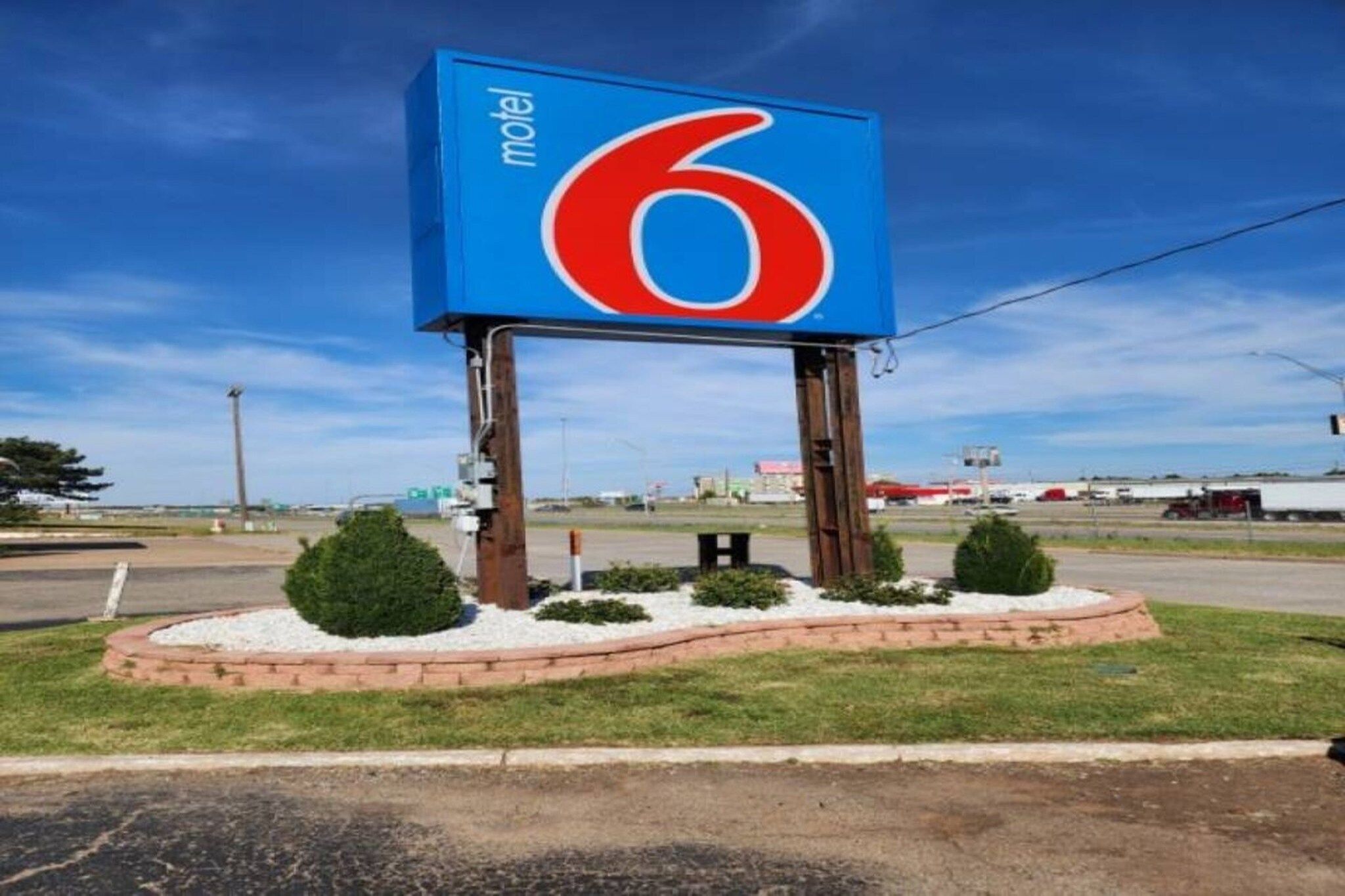 A motel sign with the number 6, surrounded by a landscaped area with shrubs and a brick border.