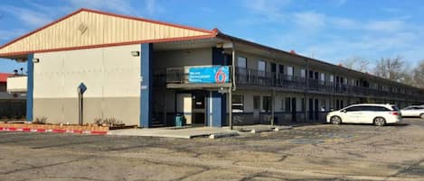 A motel with a red roof, a blue sign indicating room number 6, and a parking lot with two cars.
