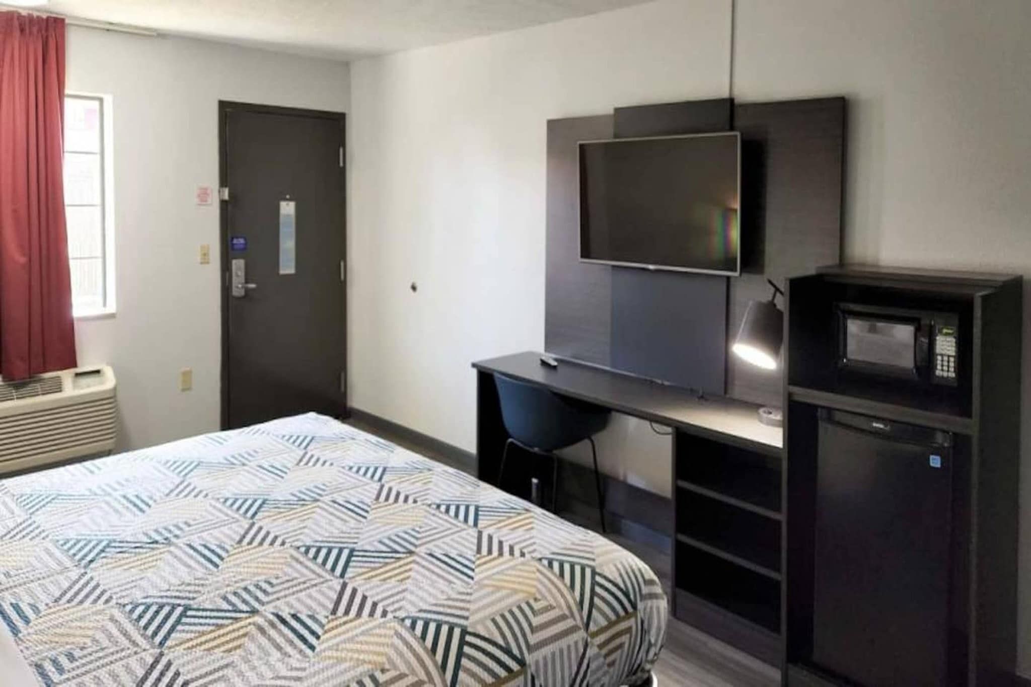 A hotel room with a bed, a desk, a television, and a microwave.