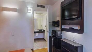 A hotel room with a TV, a microwave, and a small kitchenette area.