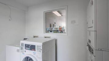 Un lavadero con lavadoras y secadoras apiladas, un espejo grande en la pared y una puerta que da a otra habitación.
