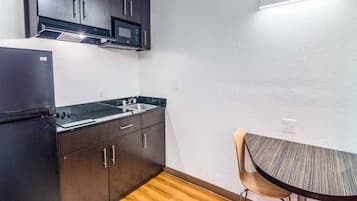 A compact kitchen with dark cabinets, a microwave, a sink, and a small dining table with a chair.