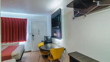 Habitación pequeña con cama, una mesa de comedor con sillas, un televisor montado en la pared y un mueble bajo.