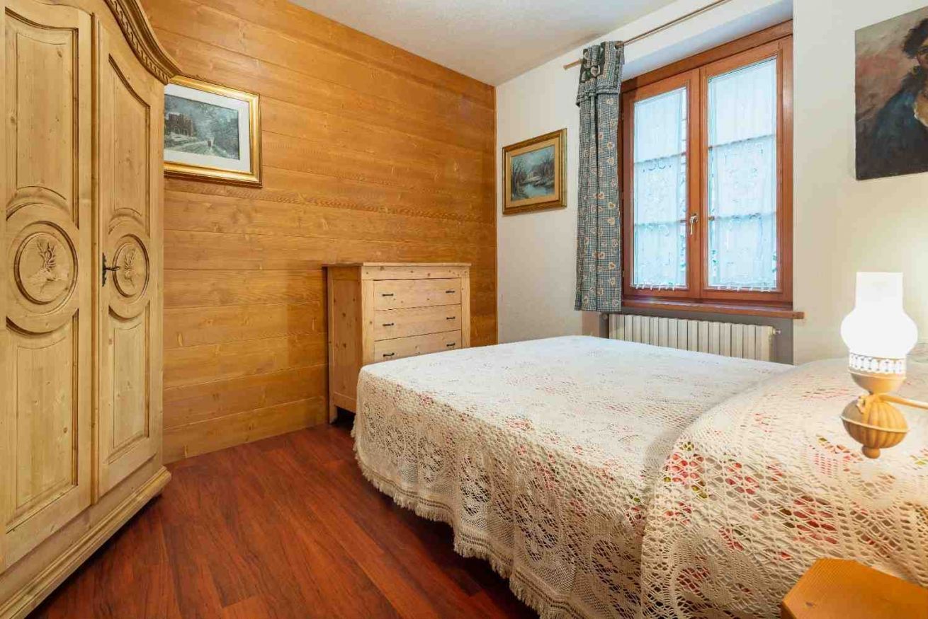 Una camera da letto con un'armadiatura in legno, un letto con coperta bianca, una cassettiera e una finestra con tende.