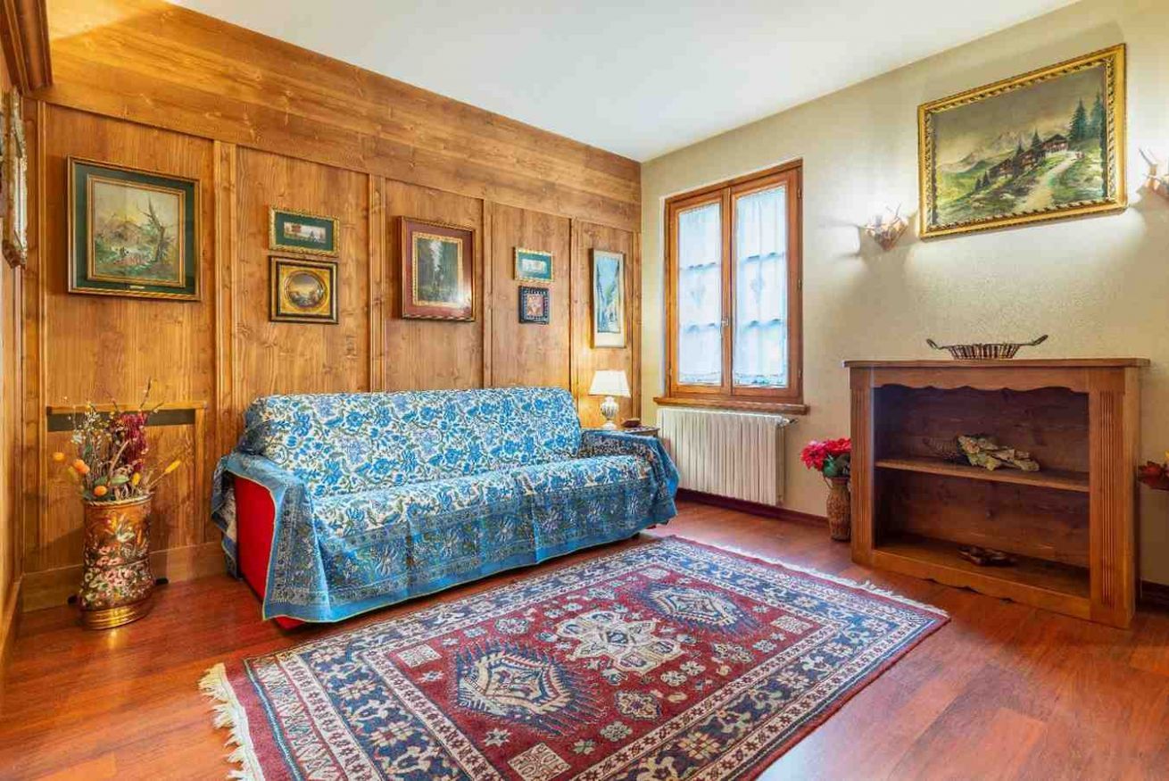 A room with a wooden paneled wall, a patterned sofa, a red rug, a fireplace, and framed pictures.