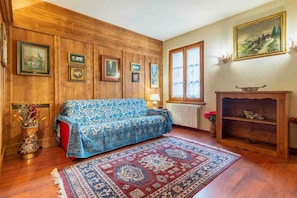 Ein Zimmer mit einer holzverkleideten Wand, einem gemusterten Sofa, einem roten Teppich, einem Kamin und gerahmten Bildern.