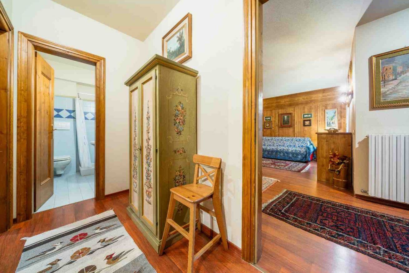 Une pièce avec un plancher en bois, une chaise, un meuble orné de motifs floraux et un lit recouvert d’une couvre-lit à motifs.