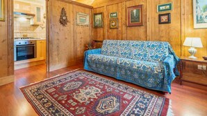 Een kamer met een bank, vloerkleed, houten wanden en een keukenhoek.