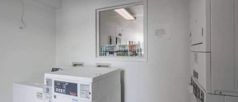 A laundry room with stacked washers and dryers, a large mirror on the wall, and a door leading to another room.