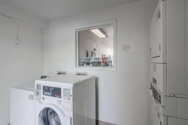 A laundry room with stacked washers and dryers, a large mirror on the wall, and a door leading to another room.