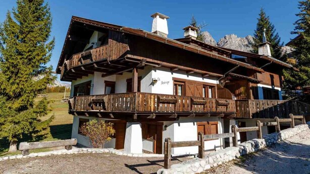 A traditional chalet with a wooden balcony, white walls, and a stone foundation. - Apartment for 5 with Panoramic Terrace Near Cortina Centre (Cortina d'Ampezzo)