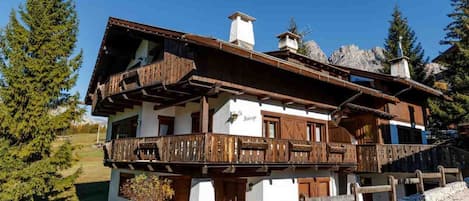 A traditional chalet with a wooden balcony, white walls, and a stone foundation.