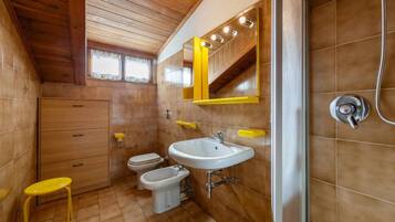 A compact bathroom with a wooden ceiling, a white sink, a toilet, and a bidet.