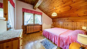 A bedroom with a wooden ceiling, a bed with pink bedding, a window with curtains, a radiator, and a wooden dresser. - Apartment for 5 with Panoramic Terrace Near Cortina Centre (Cortina d'Ampezzo)