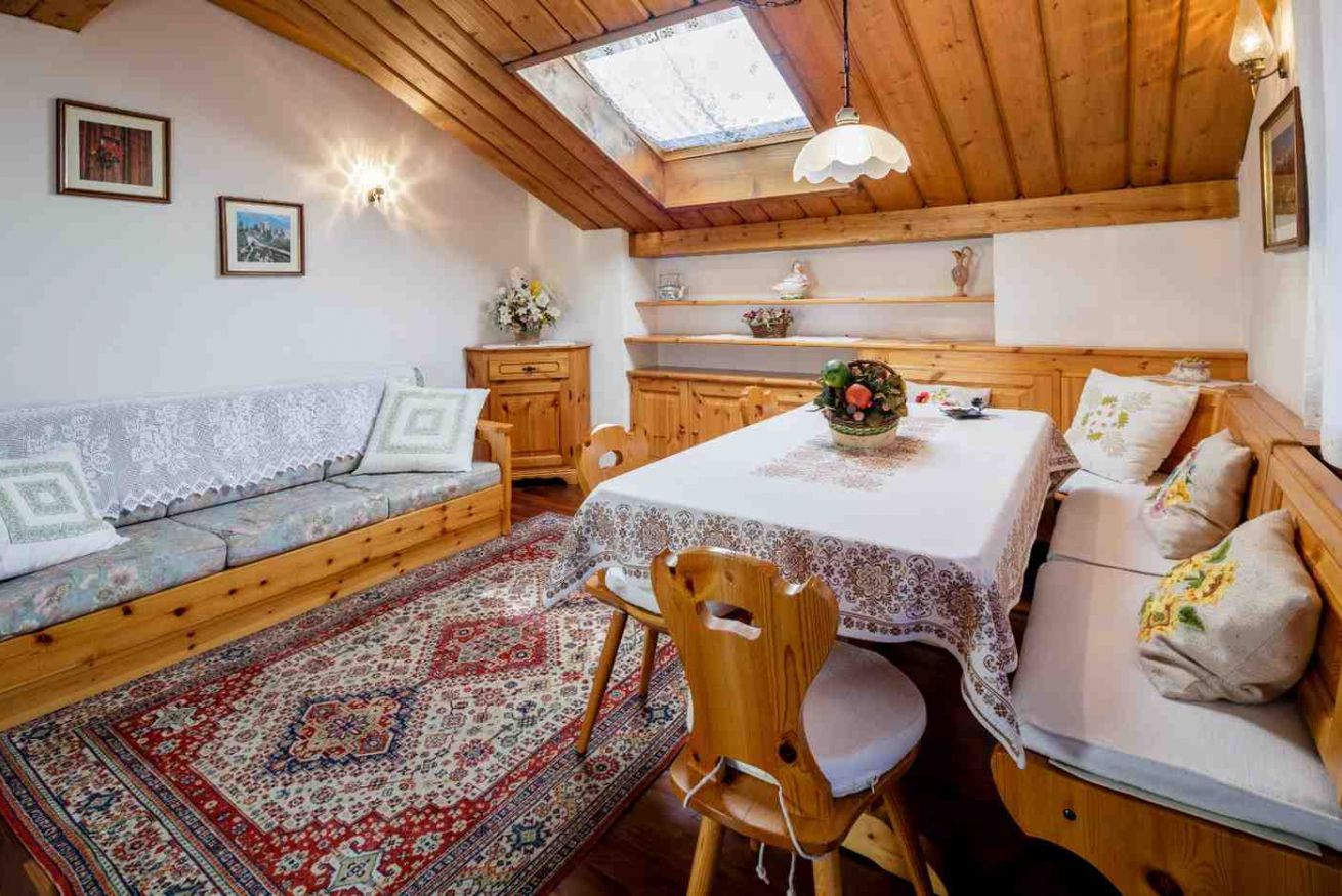 Een knus vertrek met een houten plafond, een eettafel met een kant kleed, een bank met decoratieve kussens en een traditioneel vloerkleed.