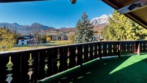 A balcony with a view of a mountain landscape, a wooden railing with decorative elements, and a clear blue sky. - Apartment for 5 with Panoramic Terrace Near Cortina Centre (Cortina d'Ampezzo)