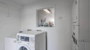 Un lavadero con lavadoras y secadoras apiladas, un espejo grande en la pared y una puerta que da a otra habitación.
