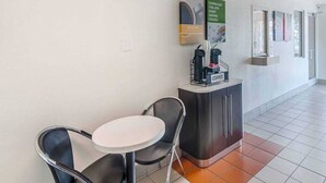 Um saguão de hotel com balcão de recepção, espaço para café e área de estar com cadeiras e mesa.