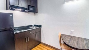 Cozinha compacta com armários escuros, micro-ondas, pia e uma pequena mesa de jantar com uma cadeira.