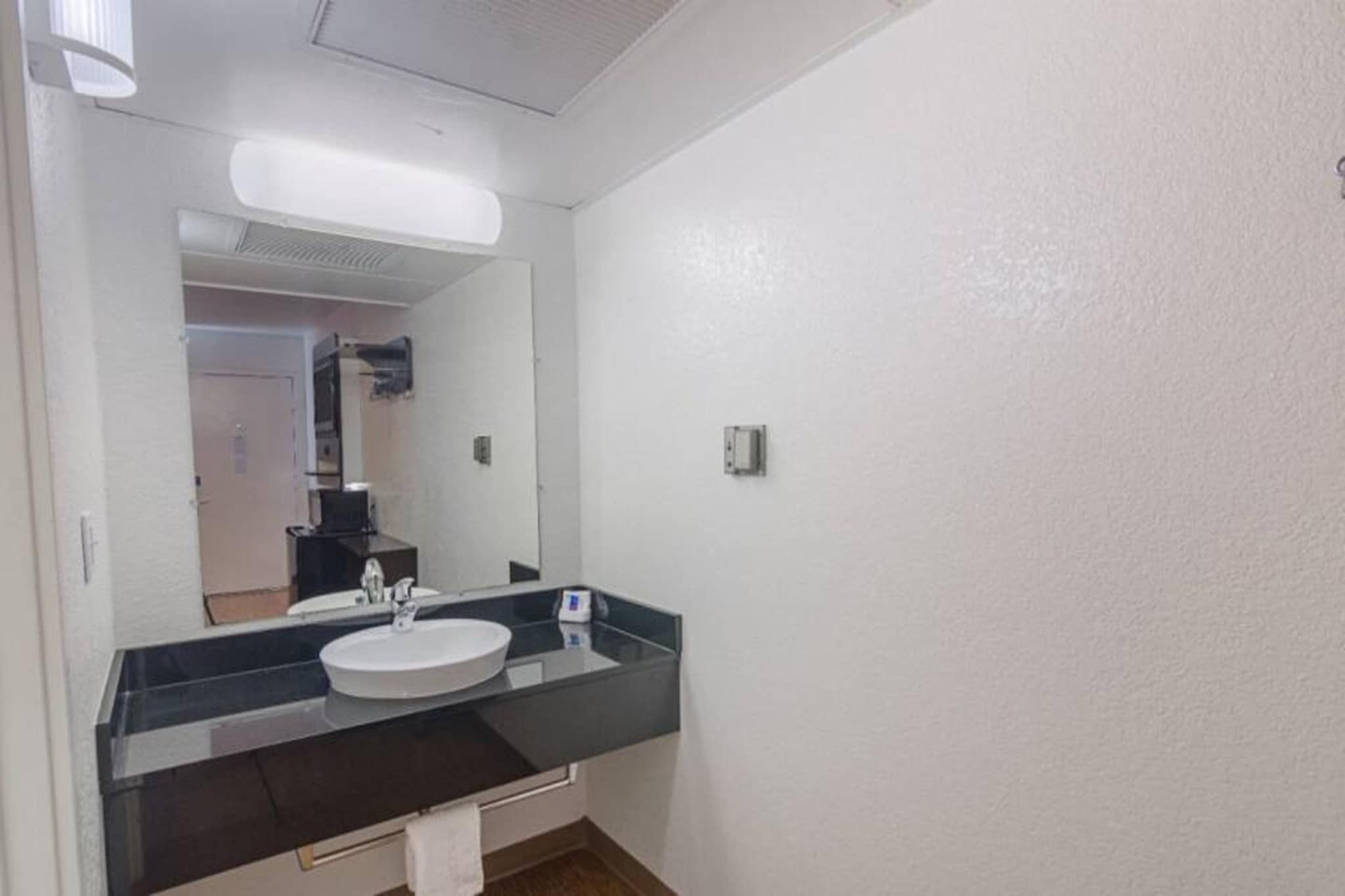 Une salle de bain avec un lavabo blanc, un miroir et un plan de toilette noir.